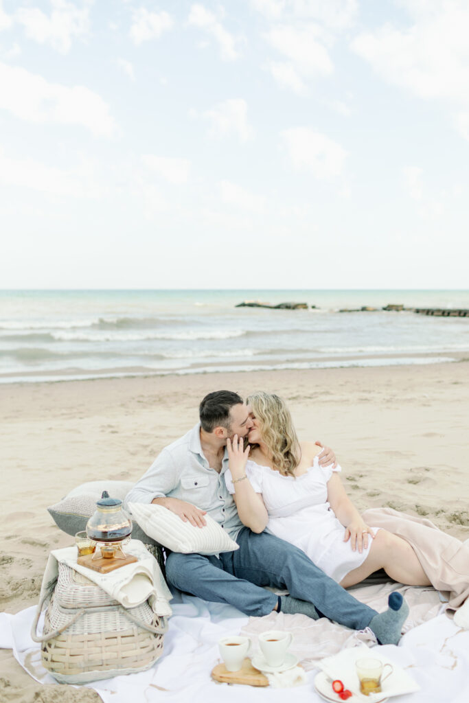 couple kissing on beach sitting on blanket