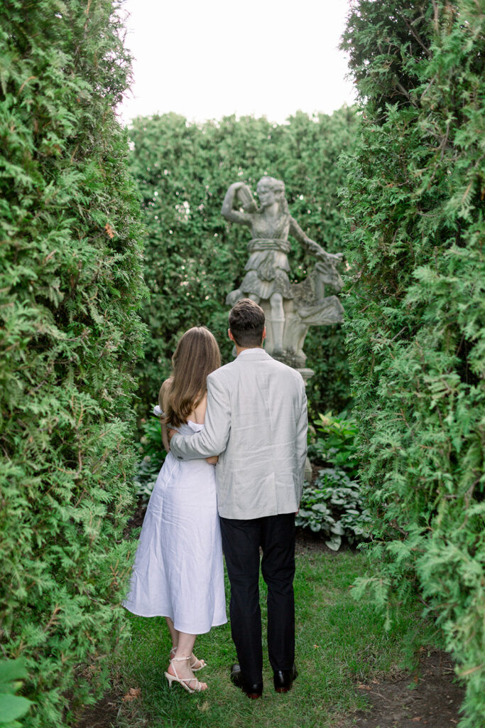 couple looking at stone statue among dense green bushes